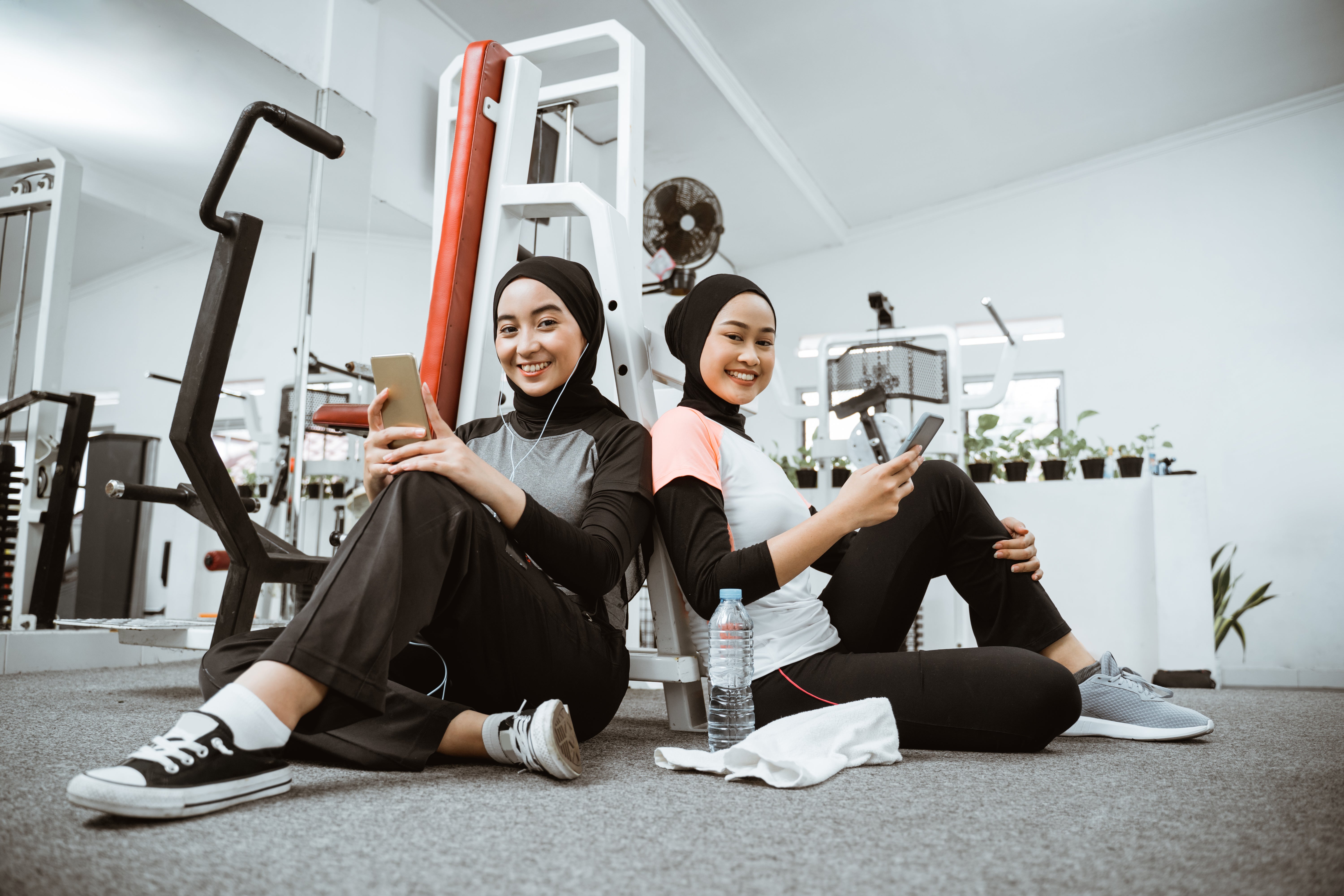 two-beautiful-muslim-sporty-woman-taking-break-after-exercising-gym-sitting-floor
